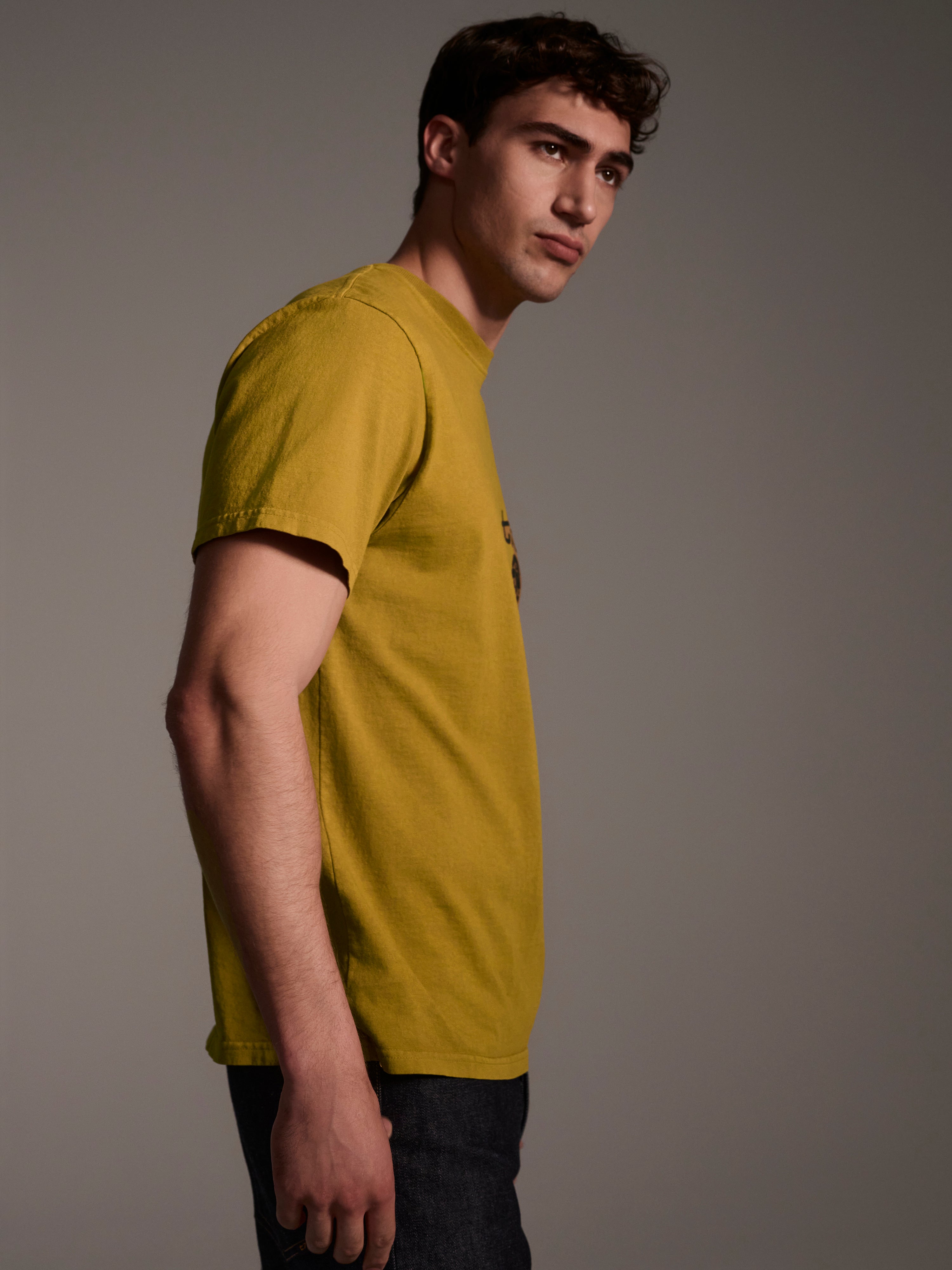 A profile image of a male model wearing a mustard t-shirt with a logo detail